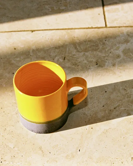Une tasse jaune et son ombre longue sur un carrelage de pierre, en plein soleil