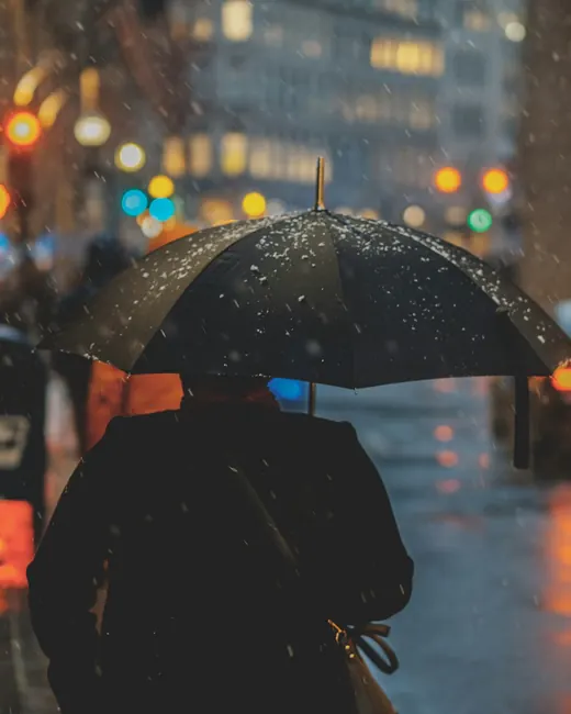 Un passant sous un parapluie, de dos, dans une rue de ville mouillée la nuit